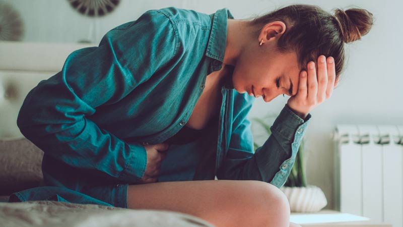 Mulher adulta com dores na zona pélvica, dobrada sobre si